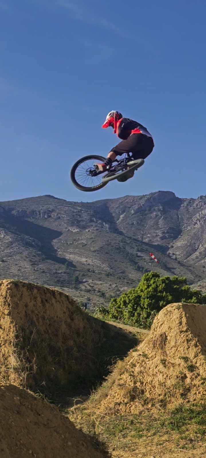 Gab pulling a whip on a dirt jump with mountains behind